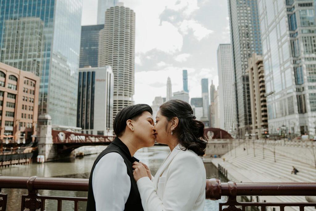 Two brides stand and kiss on Dusable bridge during their wedding portraits in the city of Chicago