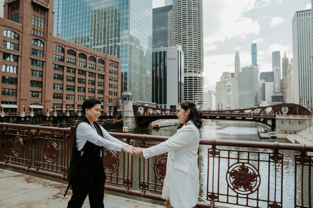 Two brides stand and hold hands on Dusable bridge during their wedding portraits in the city of Chicago