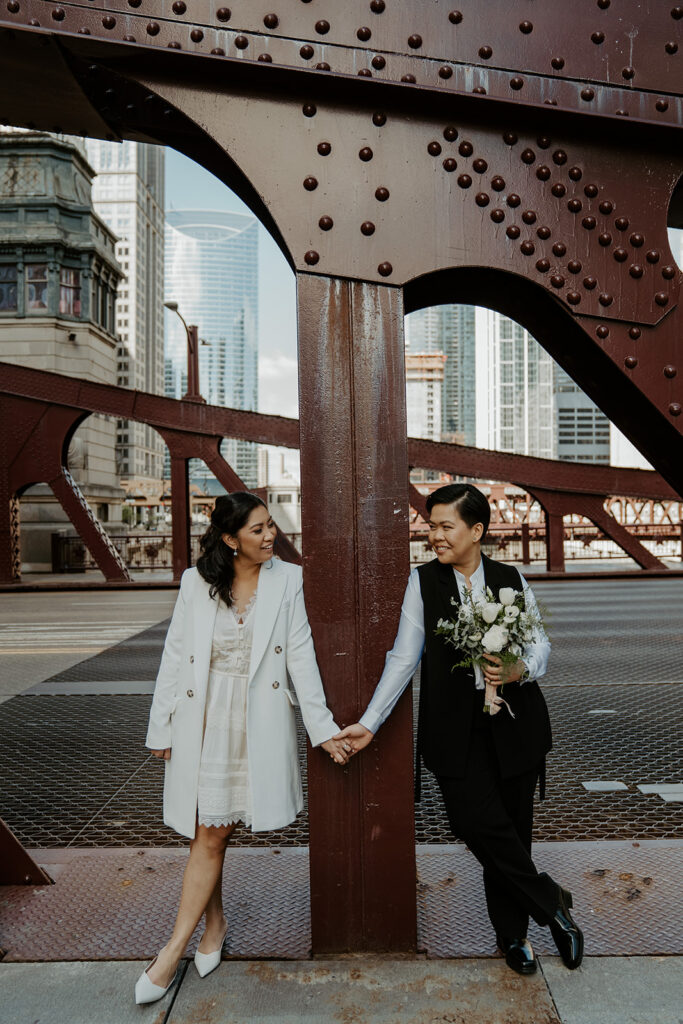 Two brides stand on Dusable bridge for their wedding portraits in the city of Chicago after their City Hall elopement.