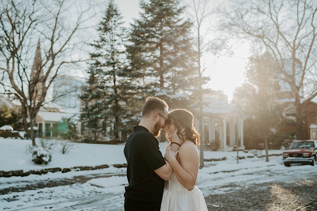 A couple smile at one another while embracing on a snowy street in Indianapolis at sunrise while taking anniversary photos