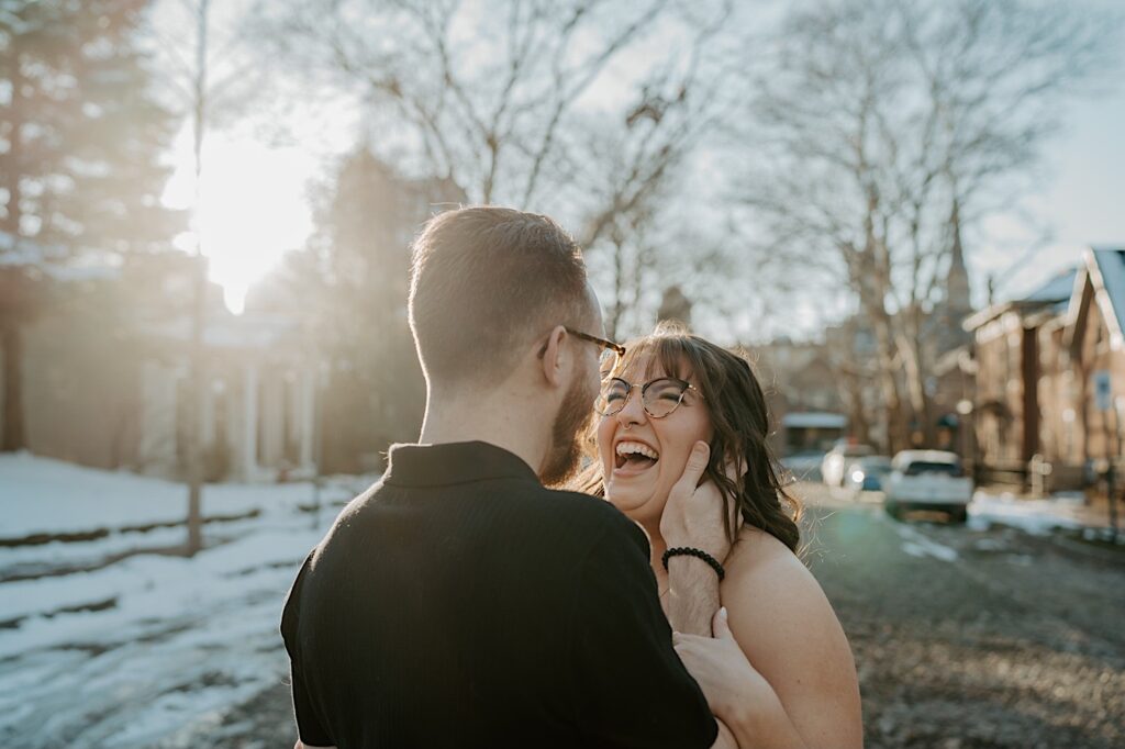 A woman smiles and laughs at a man as he holds her face while the two stand in the middle of a street in Indianapolis at sunrise while having their anniversary photos taken