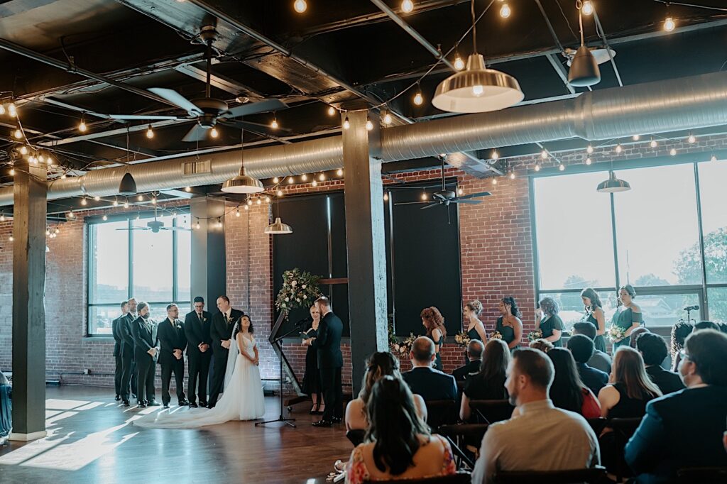 A wedding reception takes place inside of a brick building with string lights hanging from the ceiling