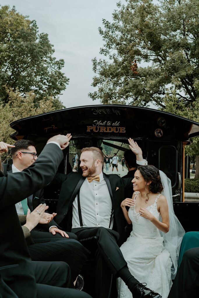 A bride and groom sit together in the back of a carriage with their wedding party members as they head to their reception