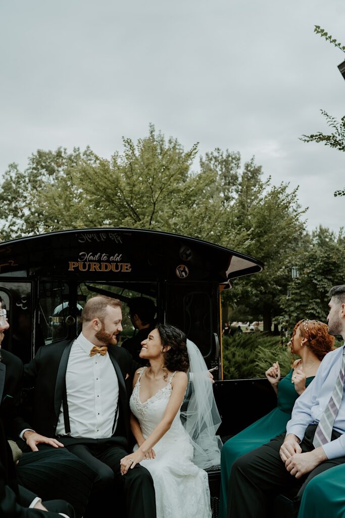 A bride and groom sit together in the back of a carriage with their wedding party members as they head to their reception