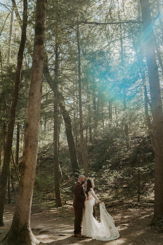 A bride and groom hold one another and lean in for a kiss while in the woods during their elopement day