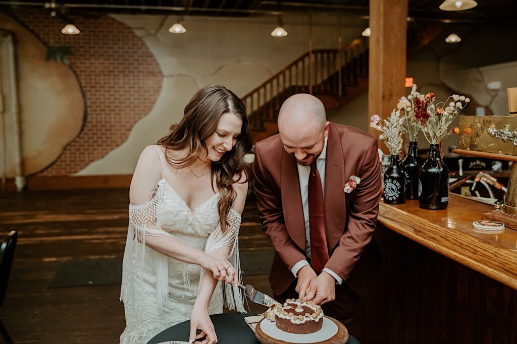 A bride and groom smile as they stand next to one another and cut their wedding cake after their elopement ceremony