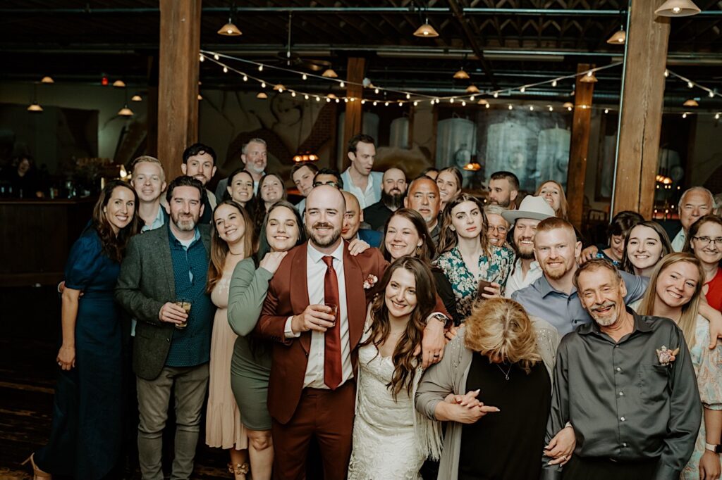 A bride and groom pose with the guests of their indoor wedding reception for a group photo
