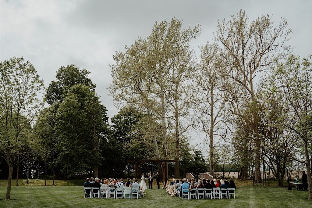 A wedding ceremony takes place in a backyard on a cloudy day
