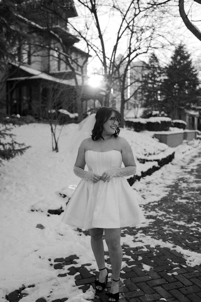 Black and white photo of a woman in a white dress standing on a snow covered sidewalk