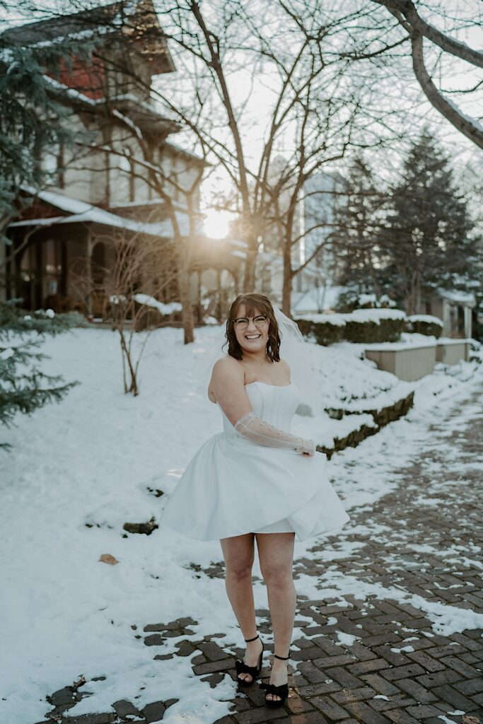 A woman dances in a white dress while standing on a snow covered sidewalk