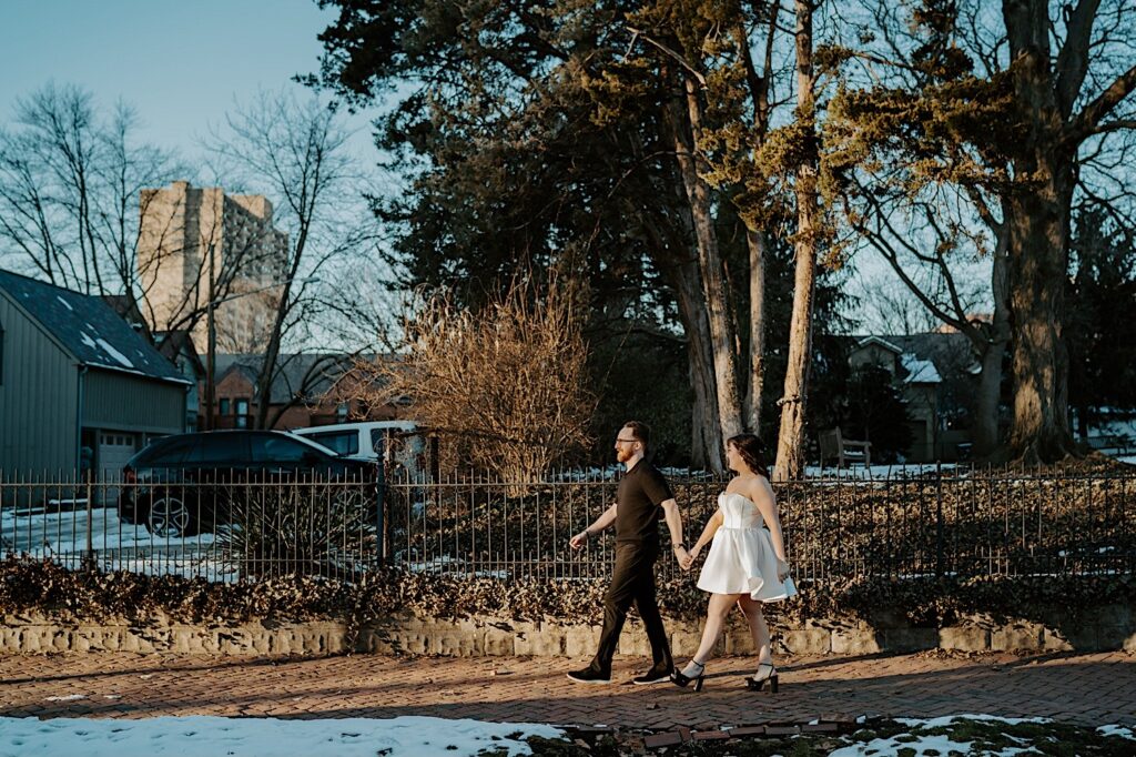 A couple walk hand in hand along a sidewalk in Indianapolis while having their anniversary photos taken