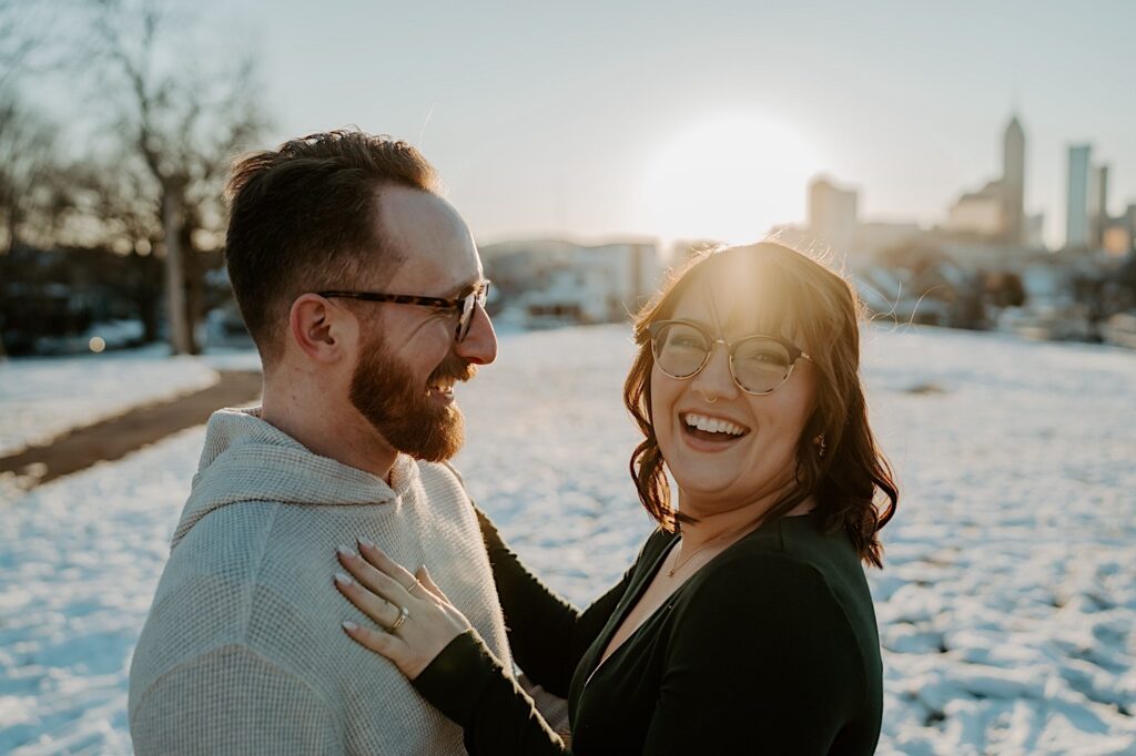 A woman smiles at the camera while a man smiles at her as they have their anniversary photos taken in a snowy field in Indianapolis at sunrise