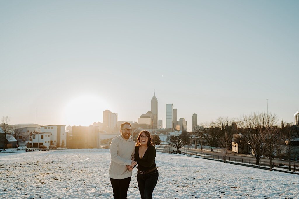 A couple smile at the camera while standing in a snowy field in Indianapolis at sunrise while they have their anniversary photos taken