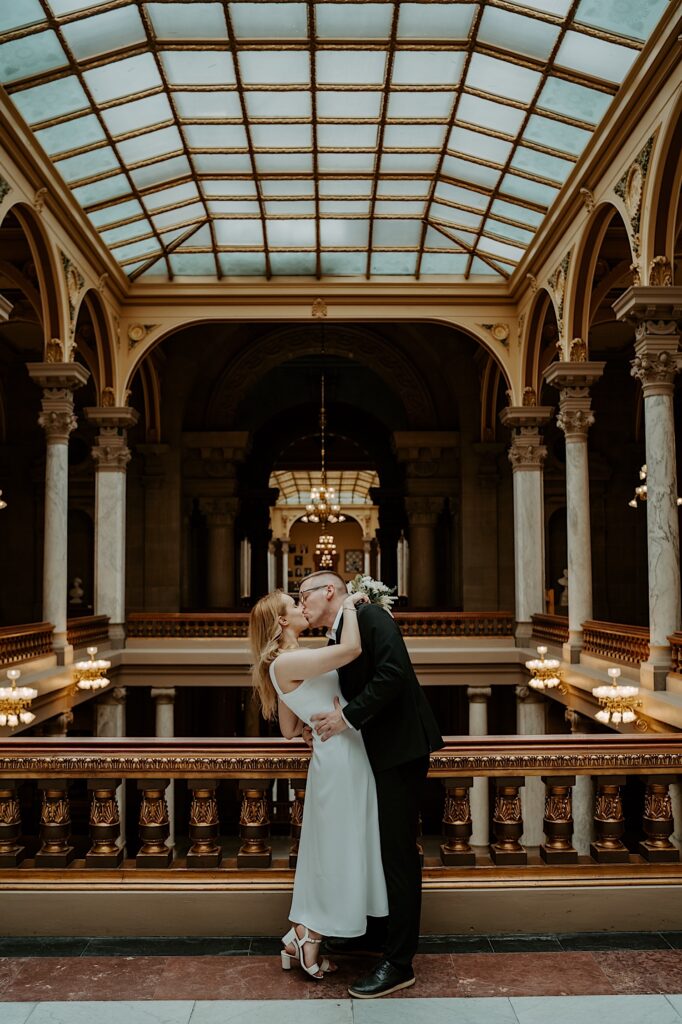 Bride and groom kiss on the top floor of the Indiana Statehouse underneath beautiful glass ceiling. 