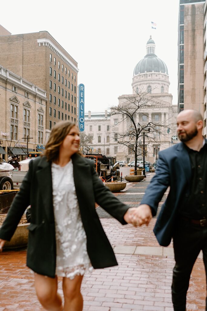 Bride and Groom hold hands running in the rain outside the Indiana Statehouse. 