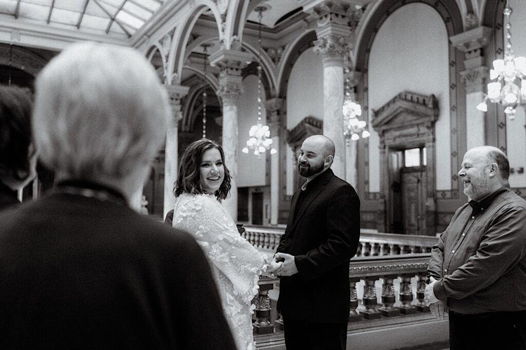 Black and White photo of Bride holding hands with groom while looking at her family during intimate wedding ceremony at the Indiana Statehouse.