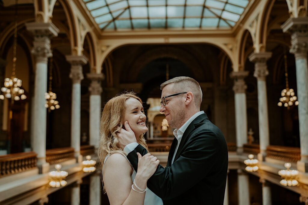 Bride giggles looking at her groom lovingly as they pose near the balcony on the top floor of the Indiana Statehouse. 