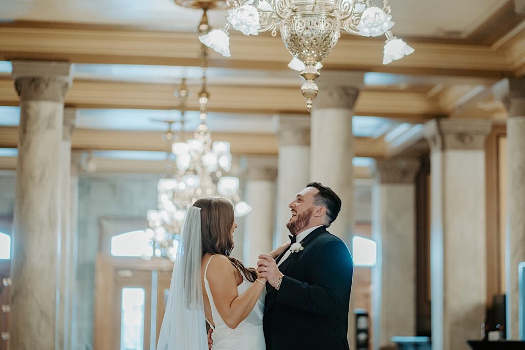Bride and groom dance underneath beautiful antique chandeliers during the reception at their Indiana Statehouse wedding. 