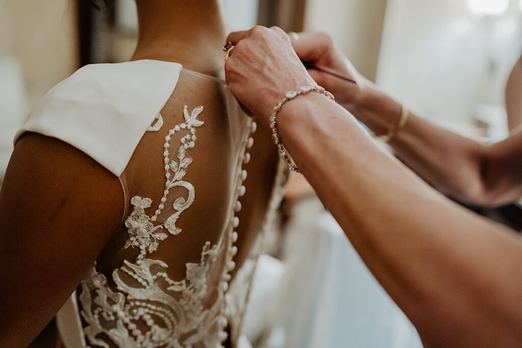 Midwest wedding Photographer captures hands buttoning the back of bride's lace dress. 