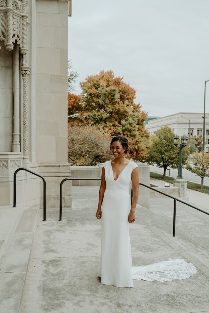 Bride in a v-neck minimal wedding dress stands outside the Scottish Rite Cathedral as her soon to be wife walks out for a first look before their LGBTQ Ceremony.