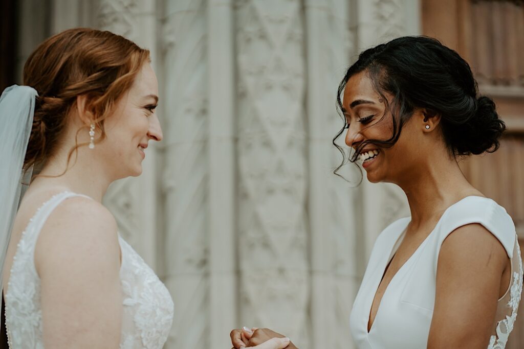 Brides hold hands and smile emotionally during their first look in front of Scottish Rite Cathedral in Indianapolis before their ceremony.