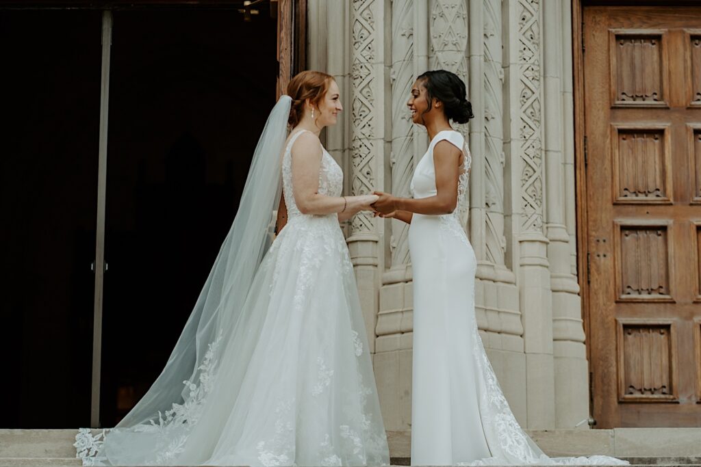 Brides stand holding hands in front of Scottish Rite Cathedral in Indianapolis before their wedding ceremony. 