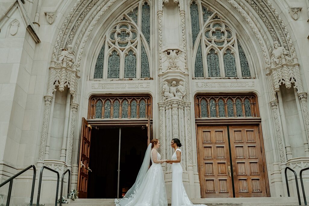 Brides hold hands and smile emotionally during their first look in front of Scottish Rite Cathedral in Indianapolis before their ceremony.