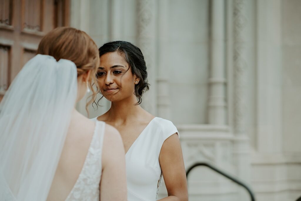 Midwest Wedding photographer captures the back of bride's head with her veil flowing behind her while the other bride's face smiles looking into her soon to be wife's eyes.