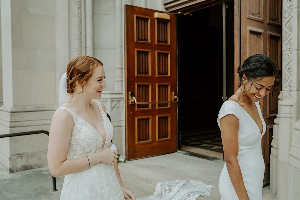 Bride smiles as her soon to be wife turns around to show off her entire gown in front of the front doors of the Scottish Rite Cathedral in Indianapolis. 