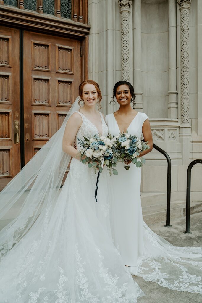 Brides stand together holding large blue and white rose bouquets as they pose for Indianapolis Wedding Photographer.