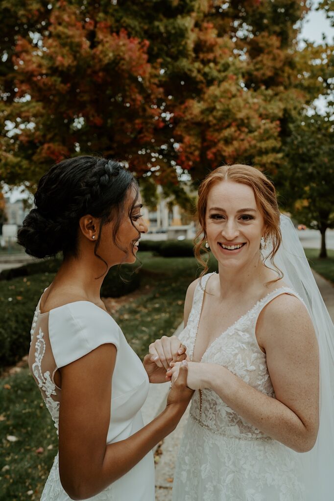 Bride with ginger hair looks into the camera as her fianceé holds her hands and looks at her. 