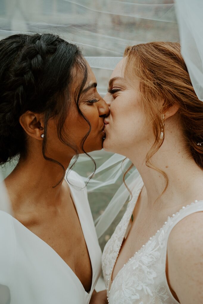 Brides kiss under white veil as Midwest Wedding Photographer captures candid wedding portraits in downtown Indianapolis. 