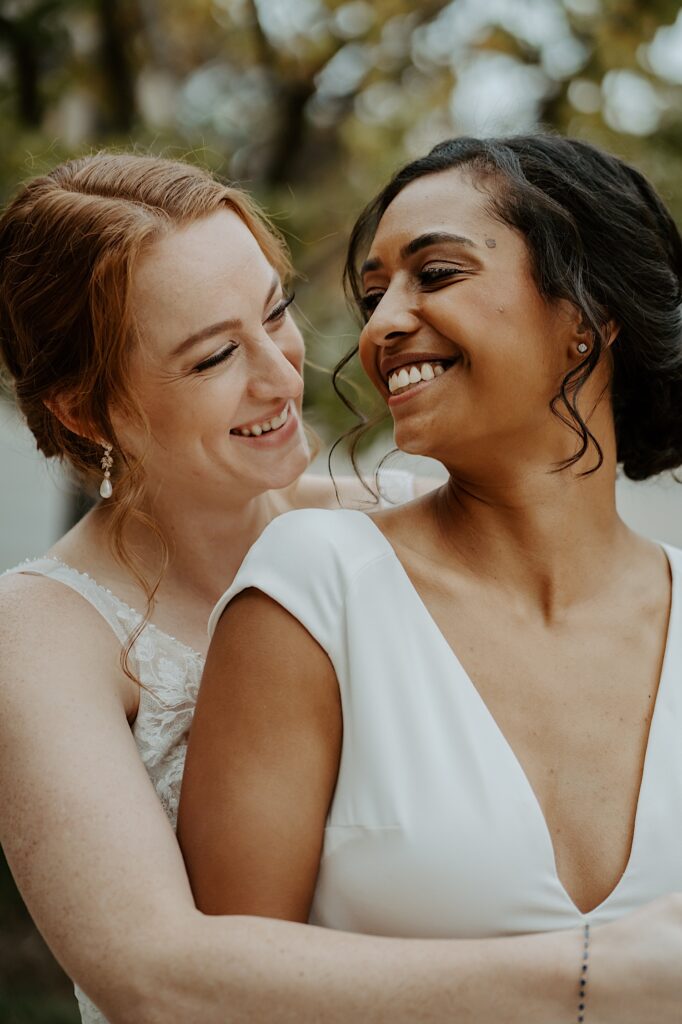 Bride is hugged from behind by her soon to be wife as she looks back at her and smiles. 