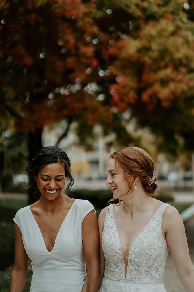 Brides in white dresses smile as they walk down the side walk. 