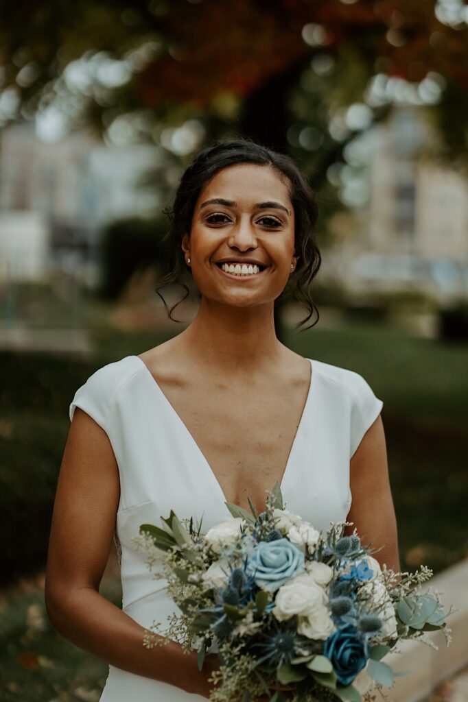 Bride smiles for the camera while holding blue and white and green floral bouquet. 