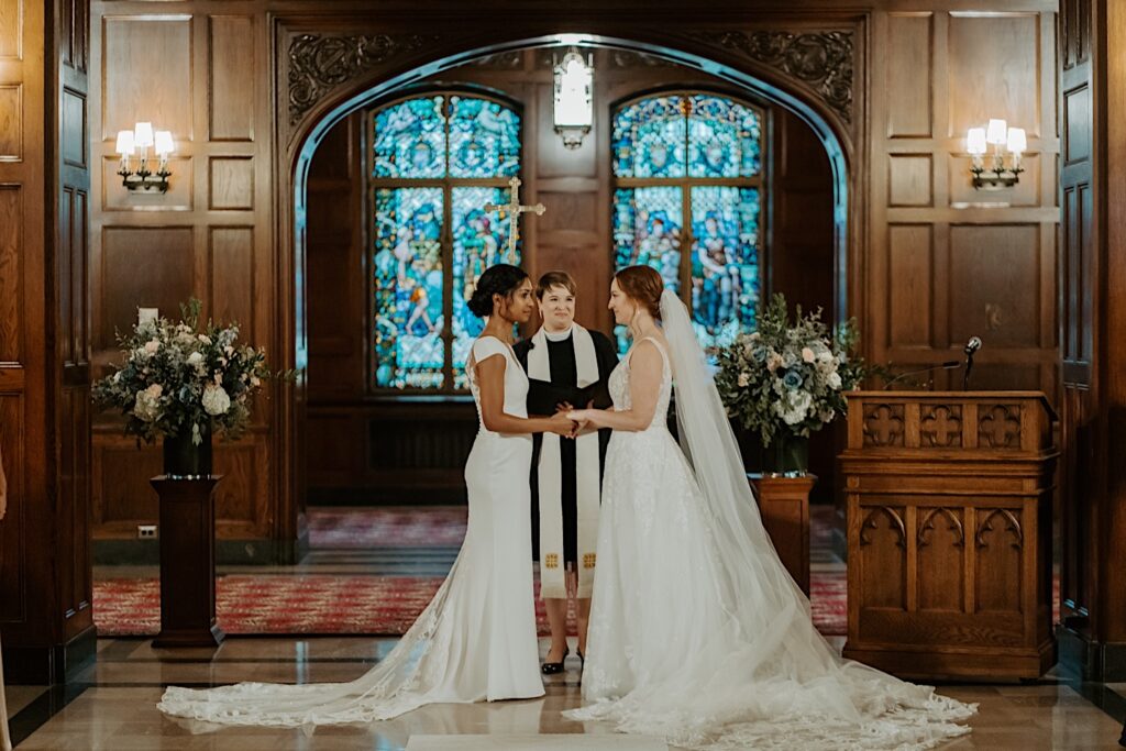 Brides stand at the end of the aisle with guests looking towards them in the Scottish Rite Cathedral in Indianapolis. 