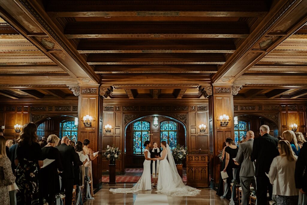 Brides stand at the end of the aisle with guests looking towards them in the Scottish Rite Cathedral in Indianapolis. 