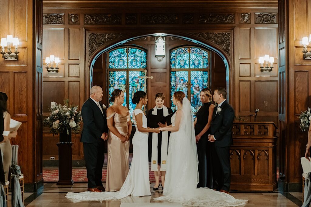 Brides stand with their parents beside them and the officiant between them during their wedding ceremony in the Scottish Rite Cathedral in Indianapolis. 