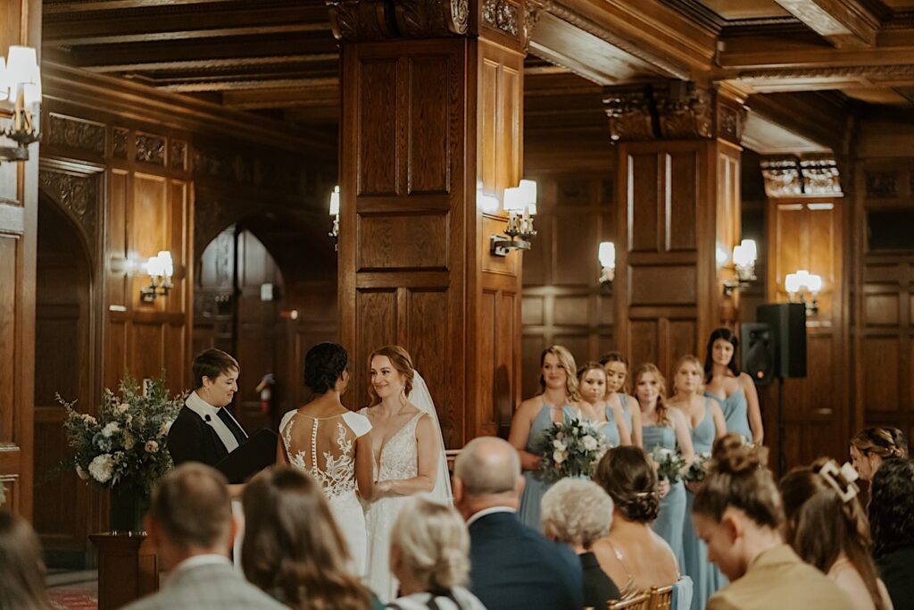 Indianapolis Wedding Photographer captures the brides at the end of the aisle with bridesmaids standing behind them wearing blue dresses in the Scottish Rite Cathedral in Indianapolis. 