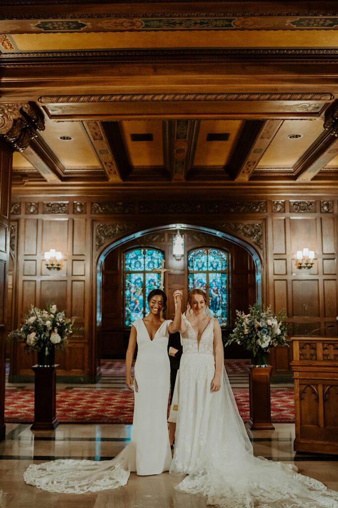 Brides hold each other's hands up and look at their guests after their ceremony.