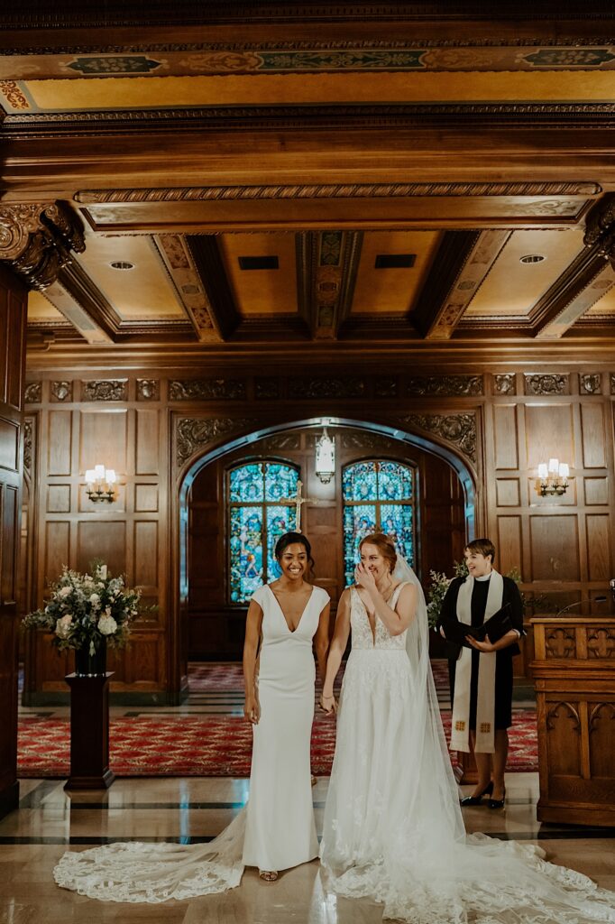 Brides hold each other's hands up and look at their guests after their ceremony.