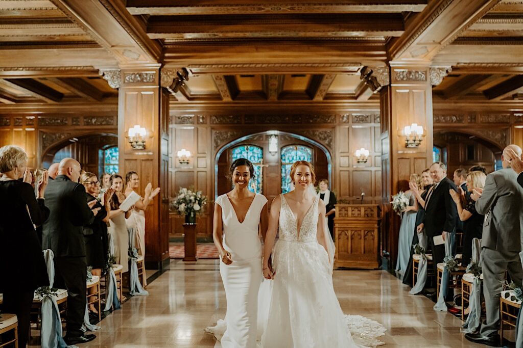 Brides walk down the aisle while their guests clap around them after their wedding ceremony in the Scottish Rite Cathedral. 