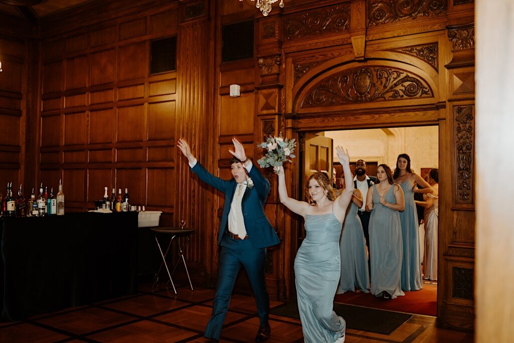 Bridesmaids and groomsmen hold their hands up as they enter the reception room at the Scottish Rite Cathedral in Indianapolis. 