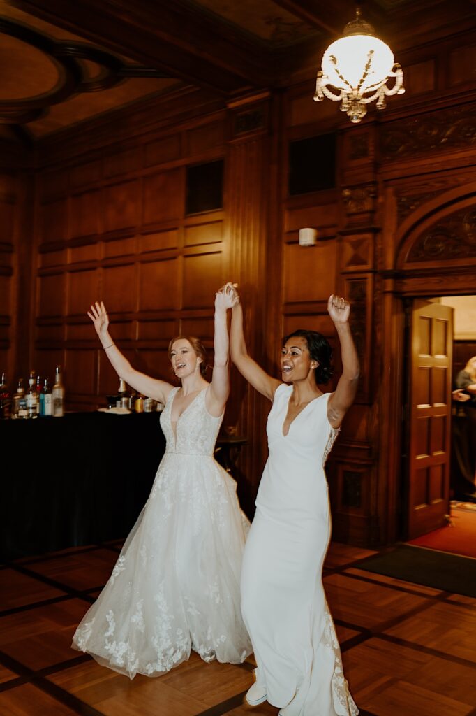 Brides hold their hands up and cheer as they enter the 1920's style  reception room at Scottish Rite Cathedral. 