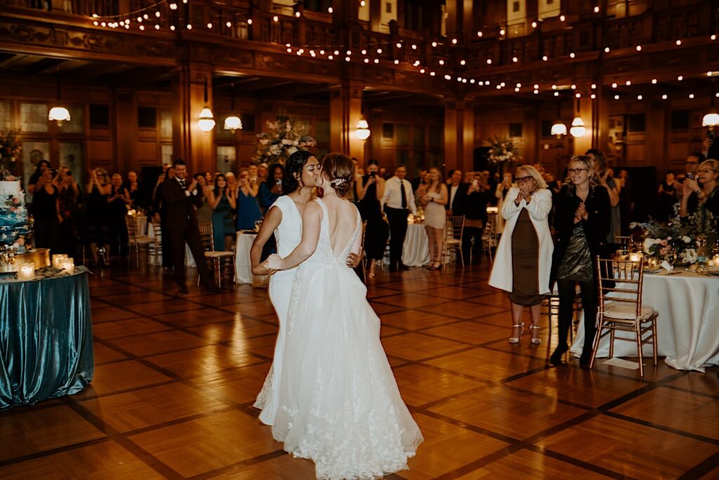 Bride's kiss as they share their first dance and their guests clap and cheer around them. 