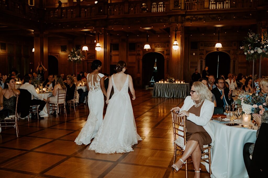 Brides walk through guests wedding tables towards their head table to sit down for dinner in 1920's reception hall. 