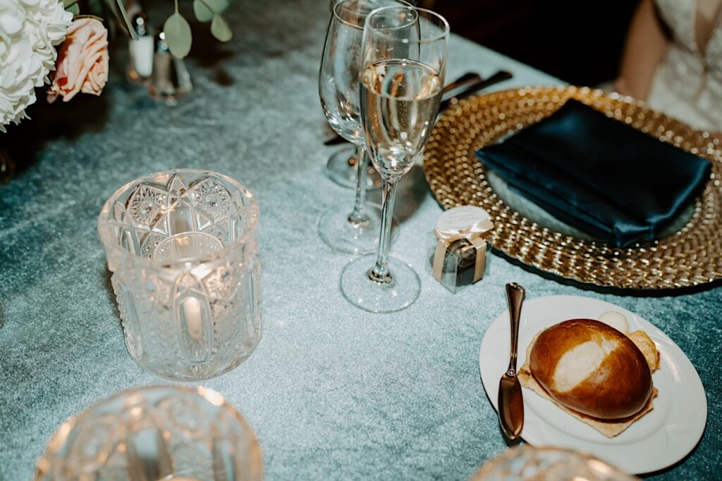 Indianapolis Wedding photographer captures wedding table with champagne glasses, bread and butter, gold chargers, all sitting on a teal blue tablecloth. 