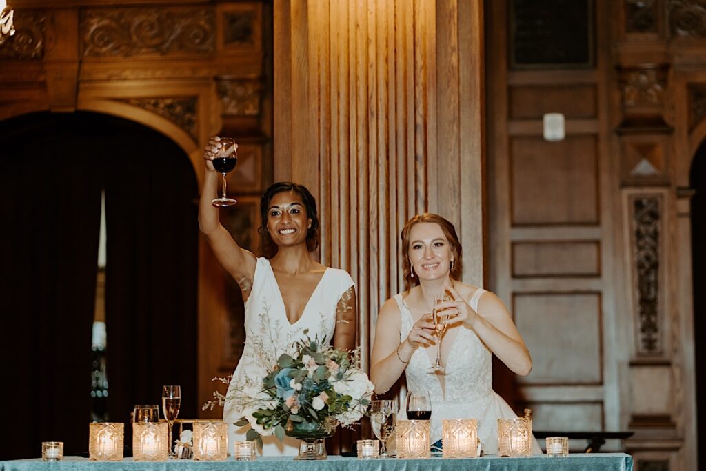 Bride's rise from their head table adorned with candles and a flower bouquet to raise their champagne glasses in the air for a toast.