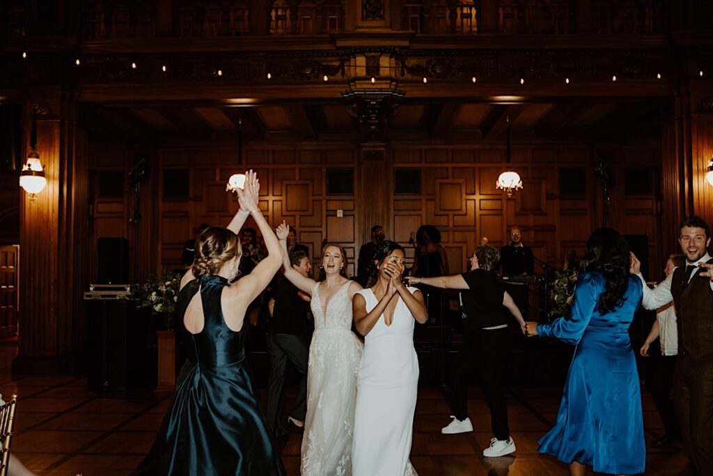 Bride's enter the reception hall at Scottish Rite Cathedral in Indianapolis as bridesmaids clap around them. 