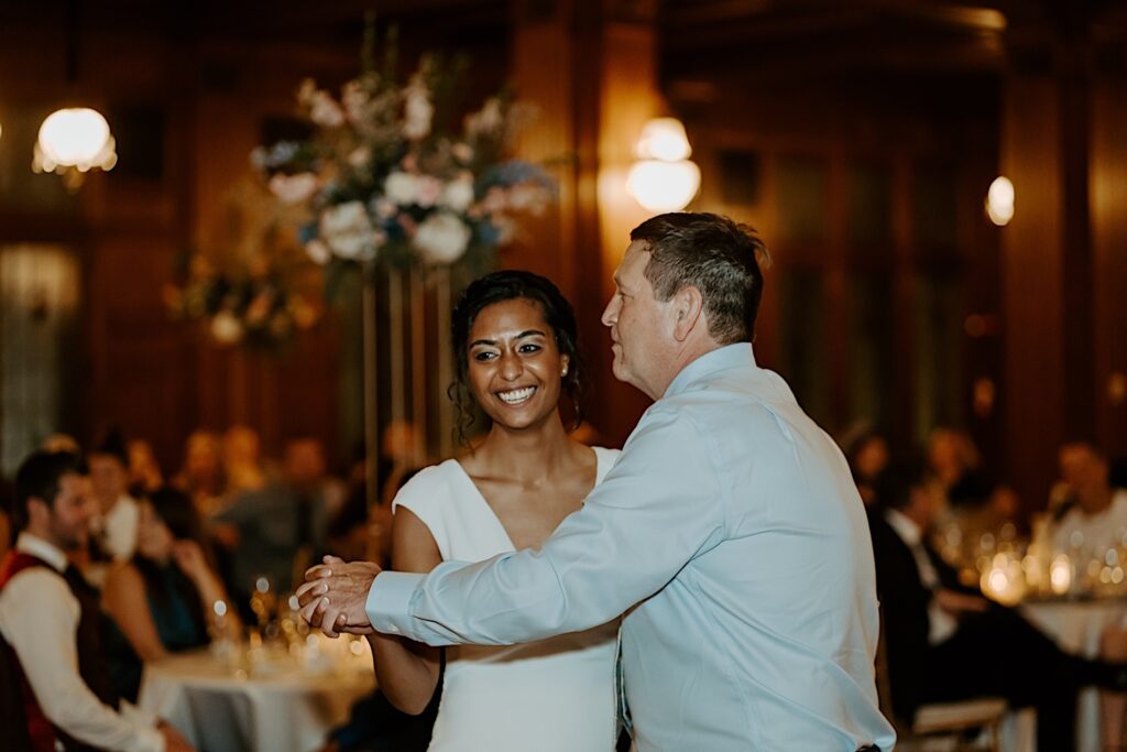 Bride dances with a man and smiles to the guests during LGBTQ+ wedding reception at Scottish Rite Cathedral in Indianapolis. 